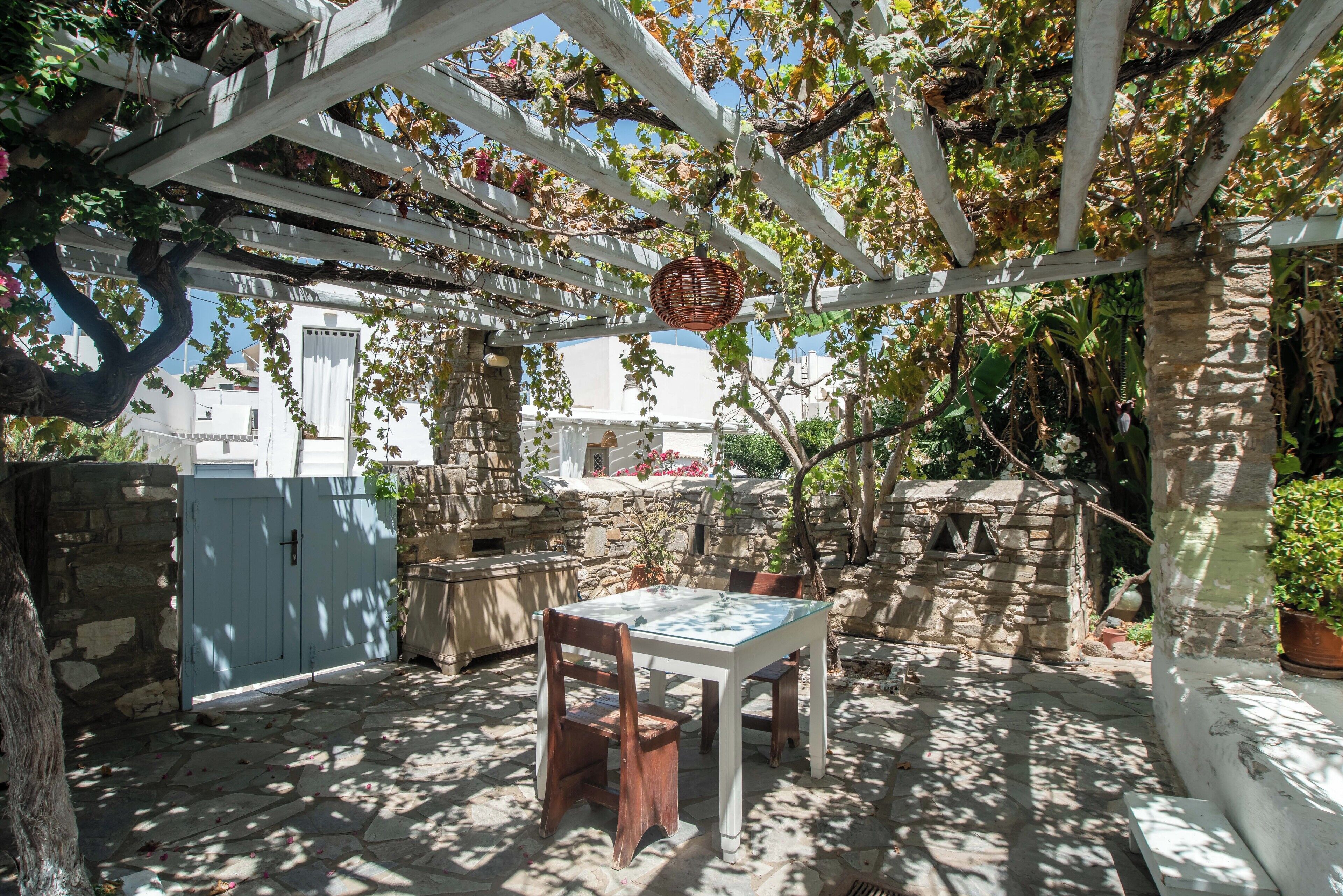 Une terrasse couverte avec une table et des chaises, des murs en pierre et une pergola recouverte de plantes grimpantes.
