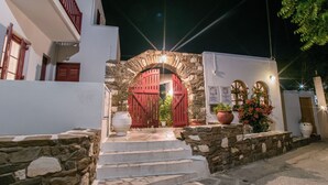 Un arc de pedra que condueix a un edifici blanc amb portes vermelles i plantes en testos.