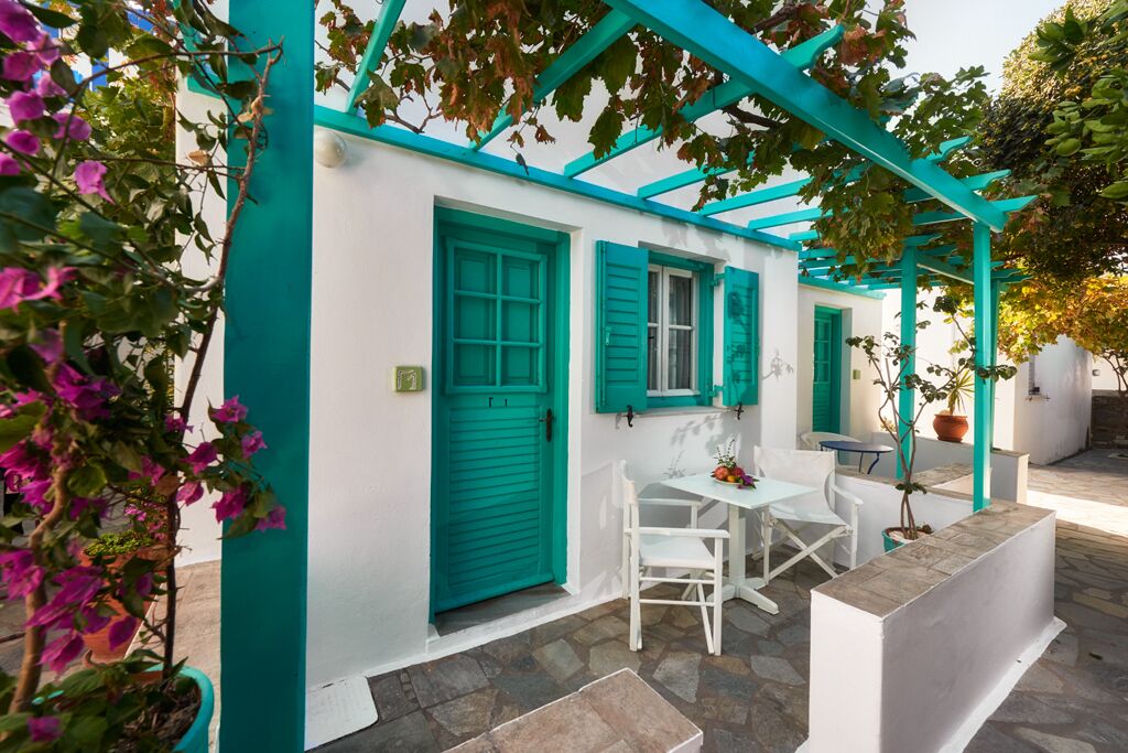 A white building with teal accents, a covered patio area with white furniture, and potted plants.