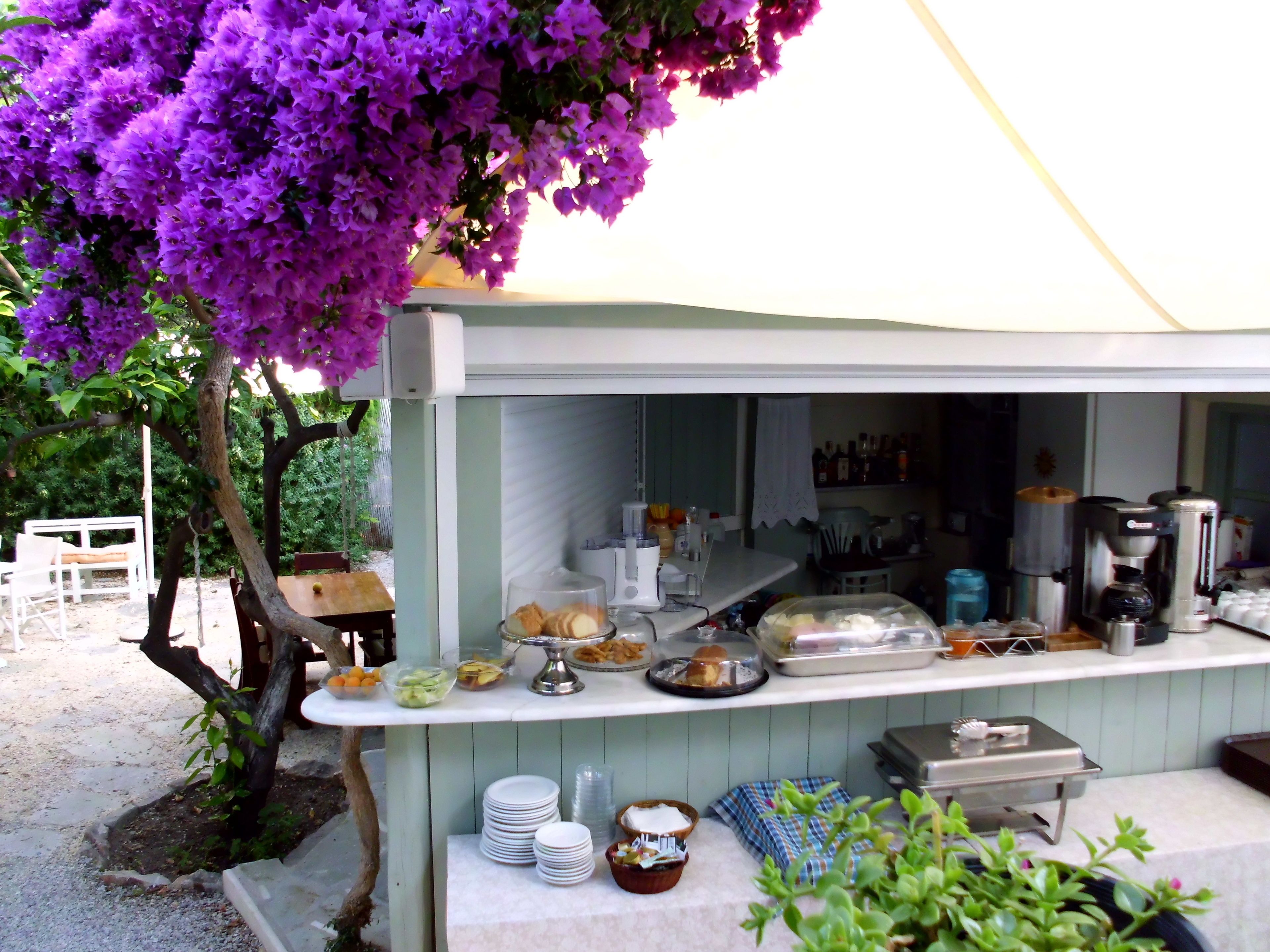 Café ao ar livre com buffet, incluindo alimentos e bebidas, sob um toldo.