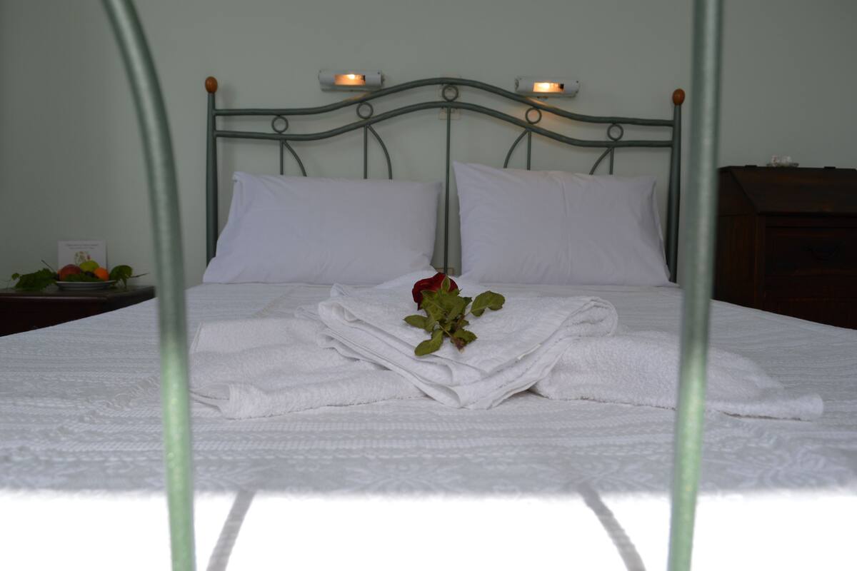 A neatly made bed with white linens and a single rose.