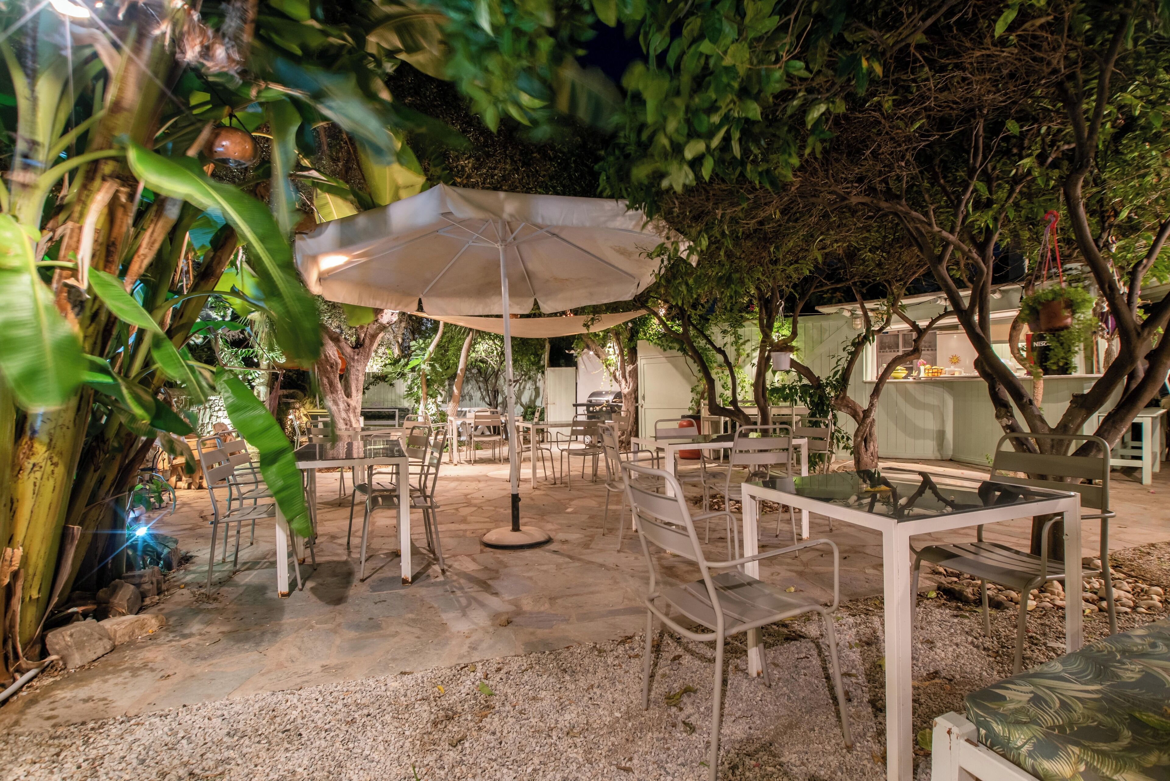An outdoor seating area with tables and chairs, surrounded by greenery and trees.