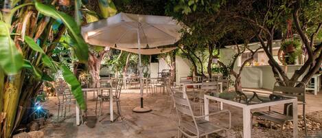 An outdoor seating area with tables and chairs, surrounded by greenery and trees.