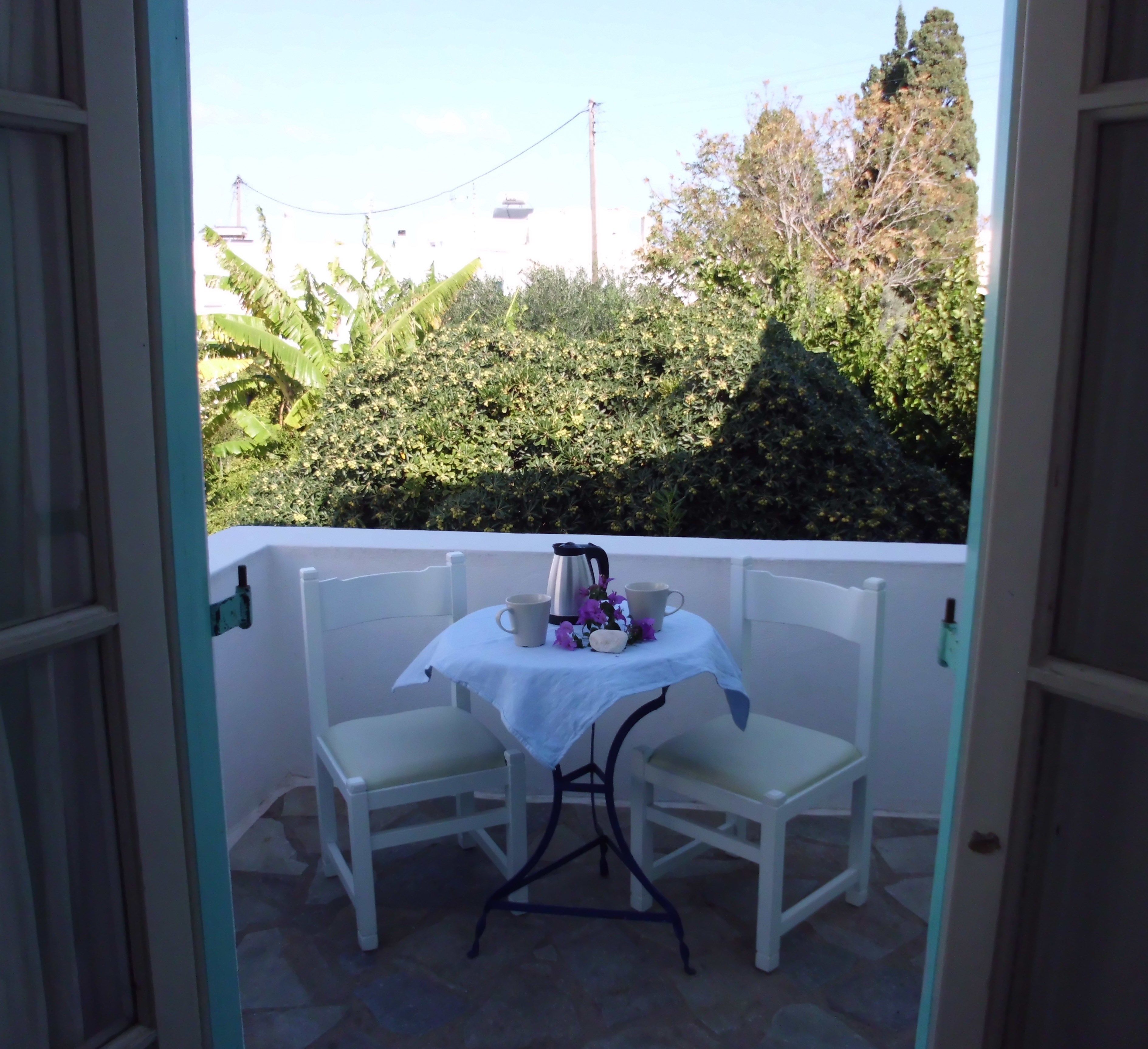 Ein kleiner Balkon mit zwei weißen Stühlen und einem Tisch, ausgestattet mit einer weißen Tischdecke und einem Wasserkocher.