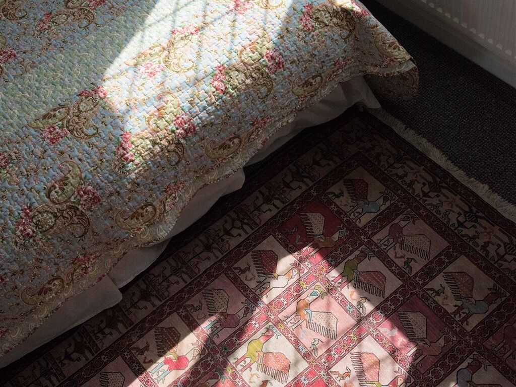 A bed with a patterned quilt and a rug with a geometric design.