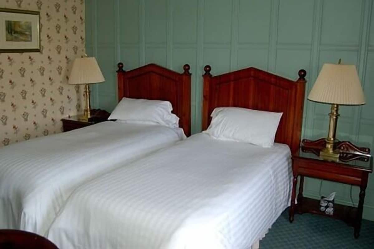 A double bed with white linens in a room with teal walls and floral wallpaper.