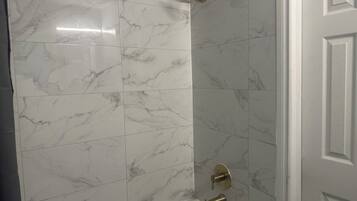 A bathroom with marble tiles, a bathtub, and a shower with a handheld showerhead.