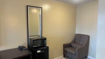 Una habitación con un refrigerador negro, un teléfono, un sillón estampado y un espejo en la pared.