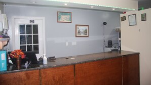 Zona de recepción con mostrador de madera, puerta blanca y cuadros en la pared.