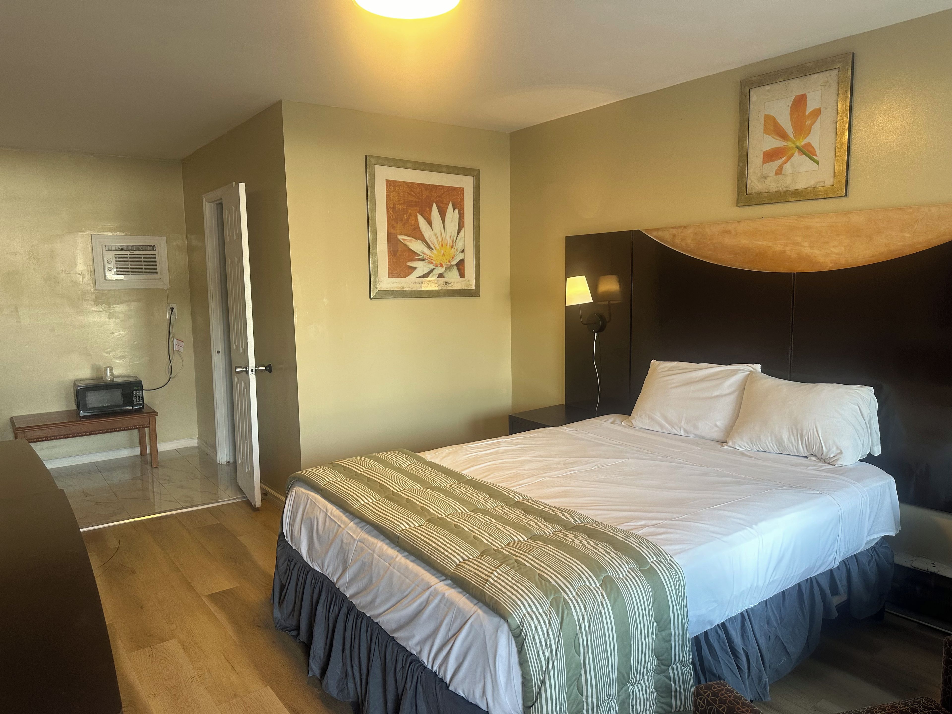 A hotel room with a bed, a bedside table, a lamp, a picture frame, and a microwave on a small table.