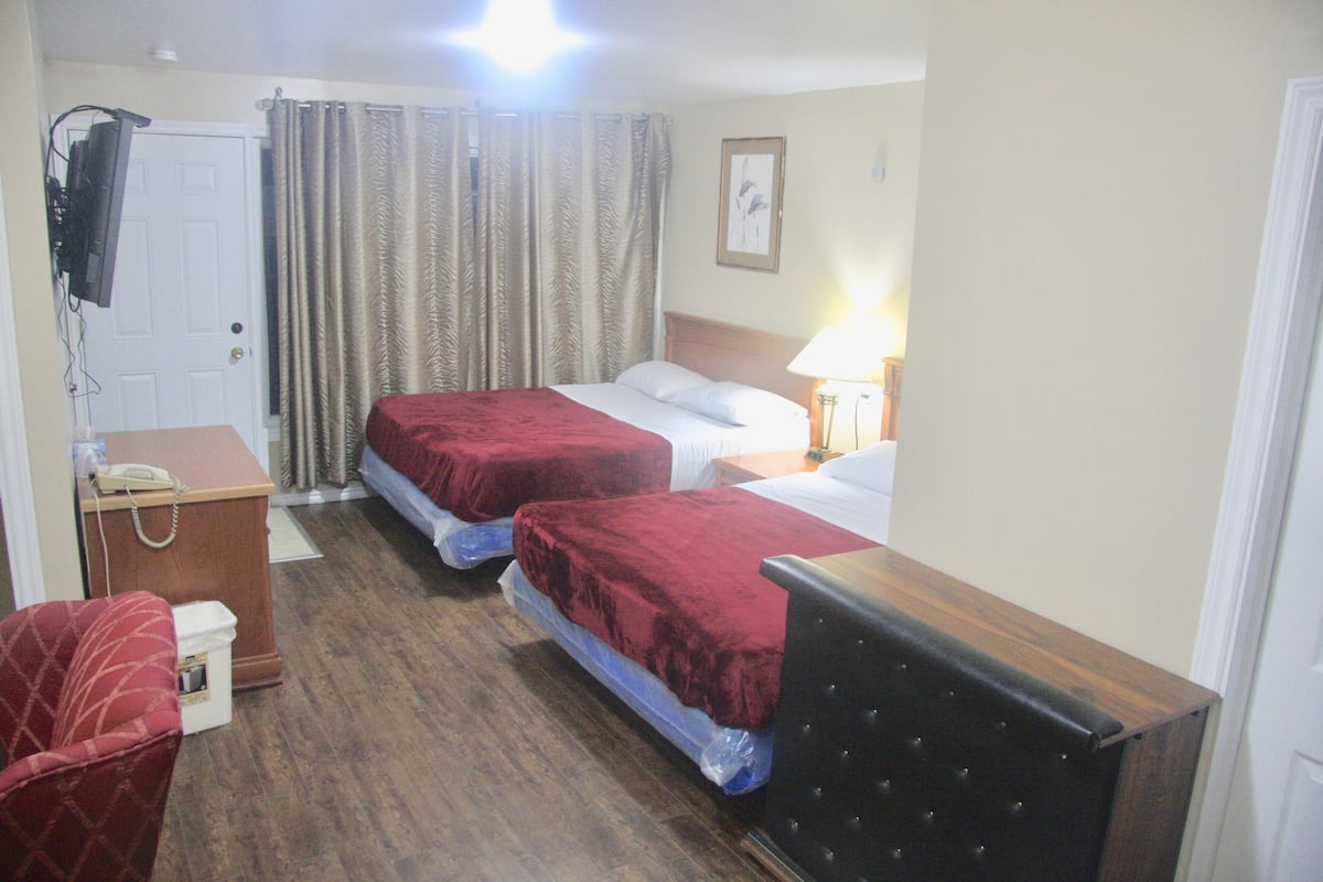Habitación de hotel con dos camas, un escritorio con teléfono, una silla y un televisor montado en la pared.