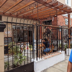 A café with a wooden pergola, a black metal fence, and a mural of a cyclist. - Hospedaje A verde (Lima)