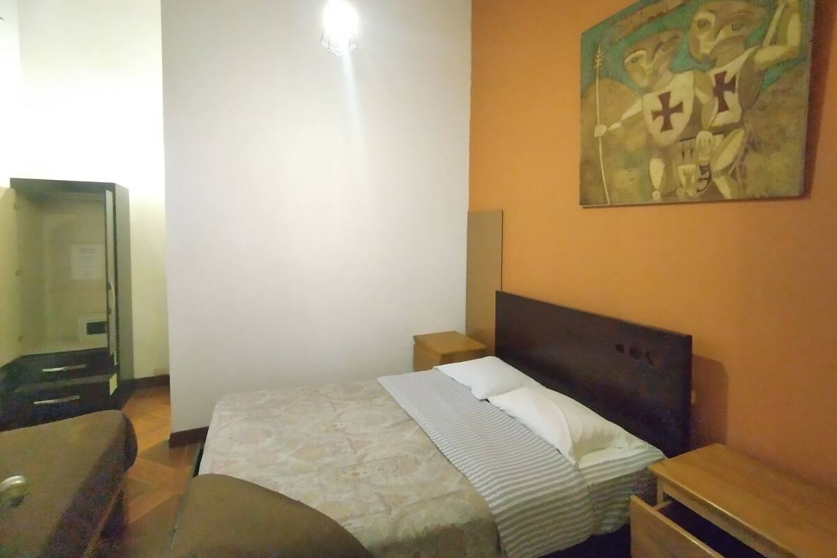 A bedroom with a bed, a nightstand, a painting on the wall, and a mirror.