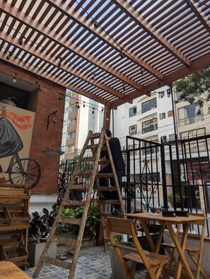 An outdoor seating area with a wooden pergola, a mural, and a ladder. - Hospedaje A Verde (Lima)