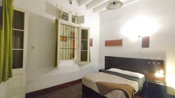 Une chambre à coucher avec un lit, une fenêtre avec des rideaux, un luminaire fixé au mur et un ventilateur de plafond.
