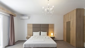 A modern bedroom with a large bed, a wooden wardrobe, a chandelier, and a bedside table with a lamp. - Oasis Exclusive  (Parga)