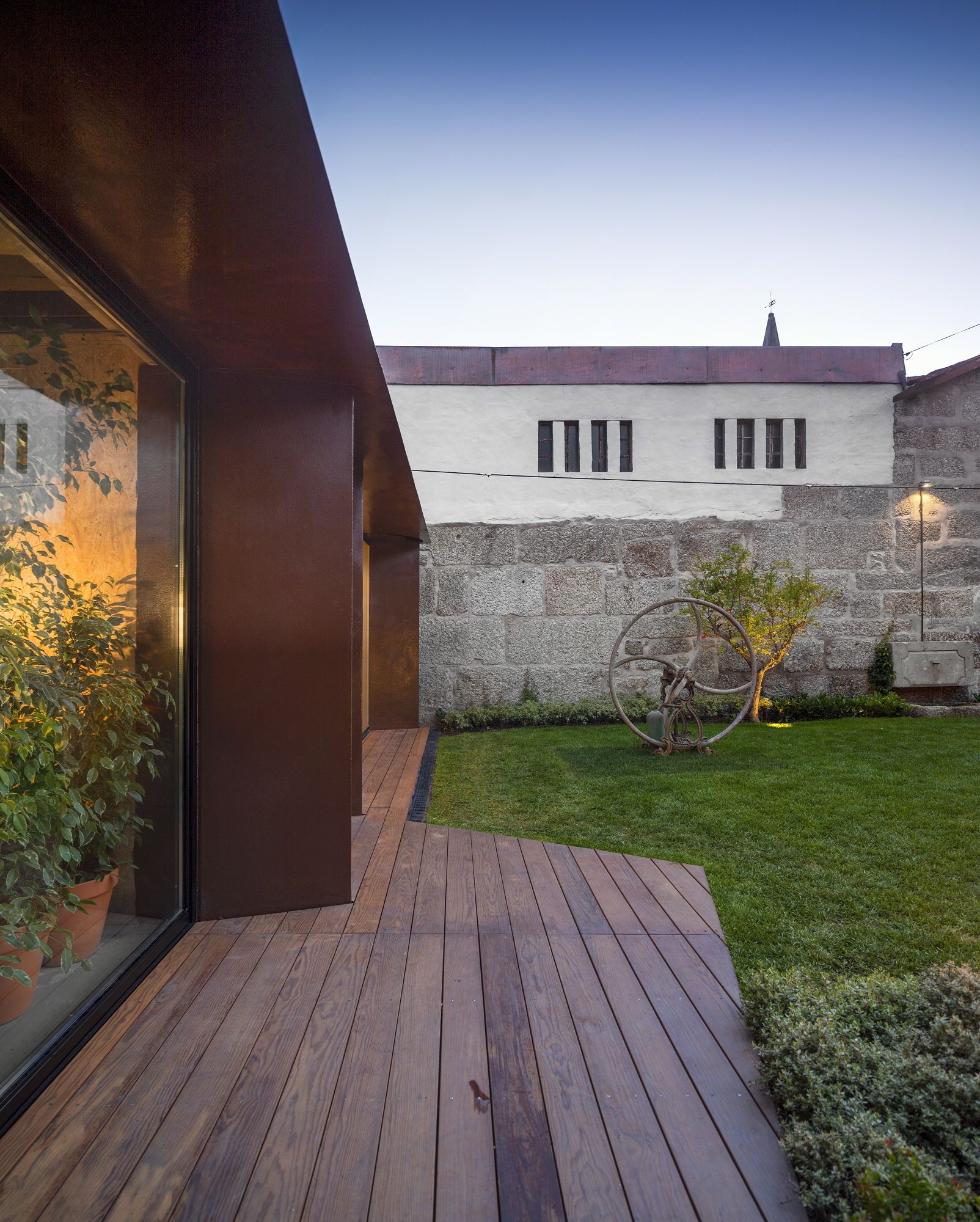 Une maison moderne avec une terrasse en bois, un petit jardin et un vélo.