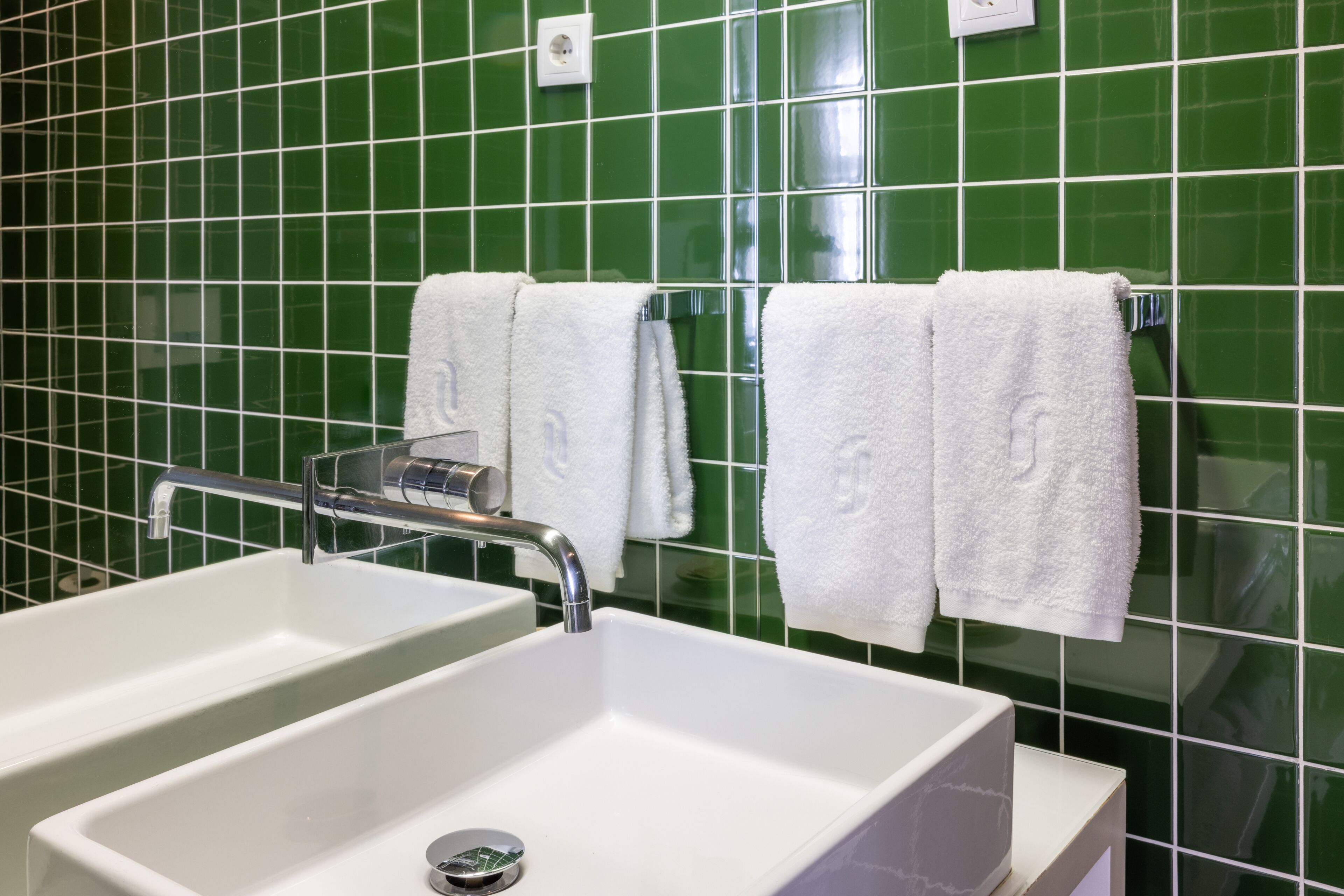 A bathroom with two sinks, a mirror, and green tiled walls.