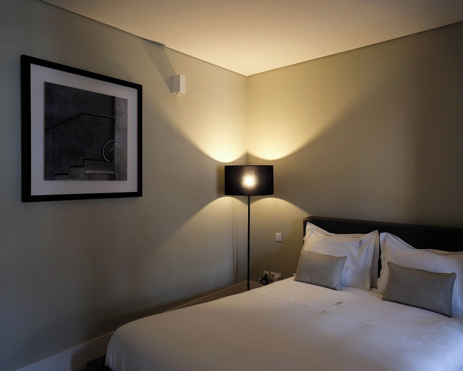 Una habitación de hotel con una cama, una mesita de noche, una lámpara y un cuadro en la pared.