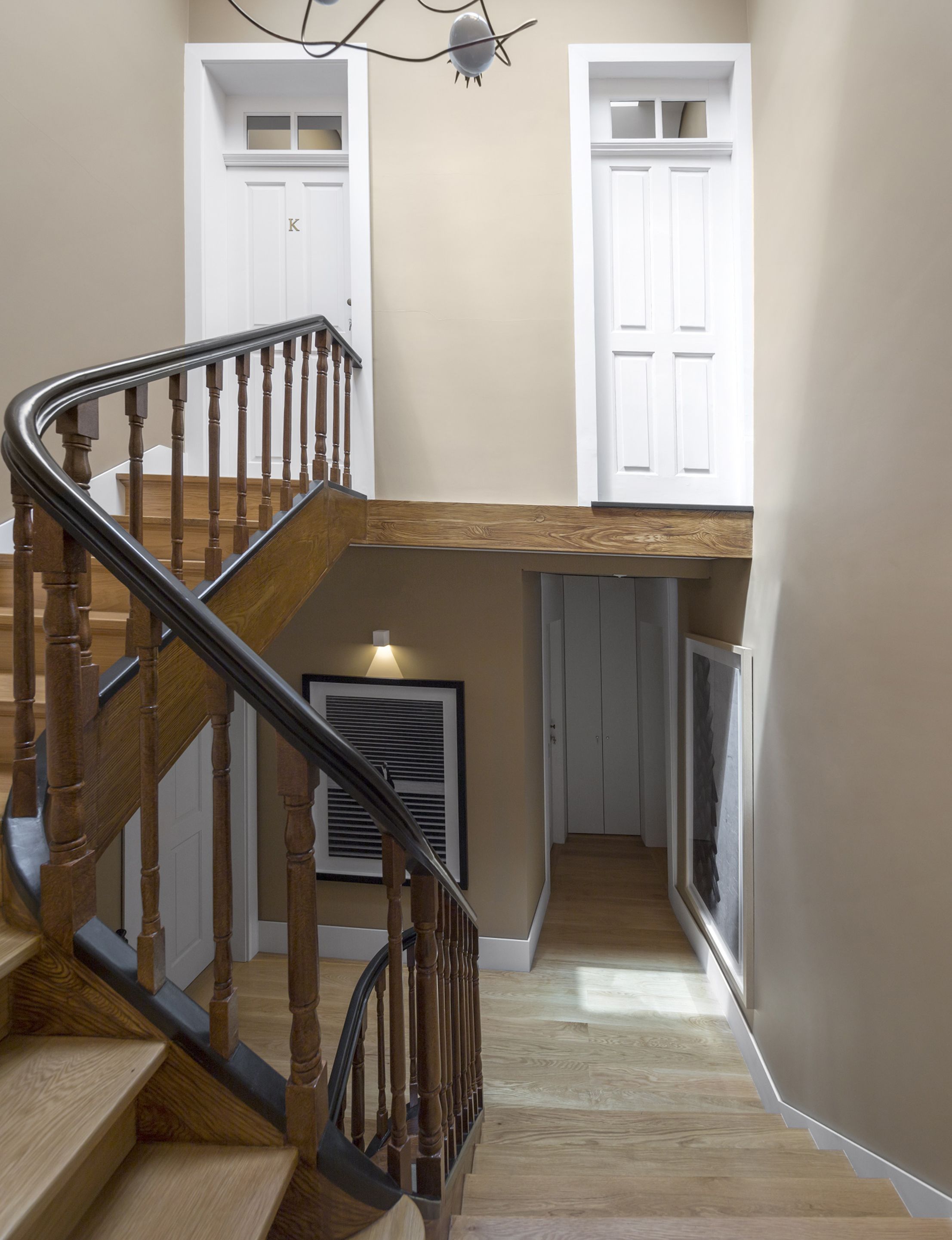 A wooden staircase with a metal handrail leading to a landing. There are two white doors on the landing, one with a window above it.