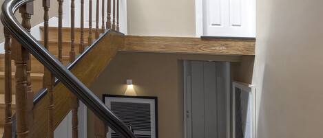 A wooden staircase with a metal handrail leading to a landing. There are two white doors on the landing, one with a window above it.