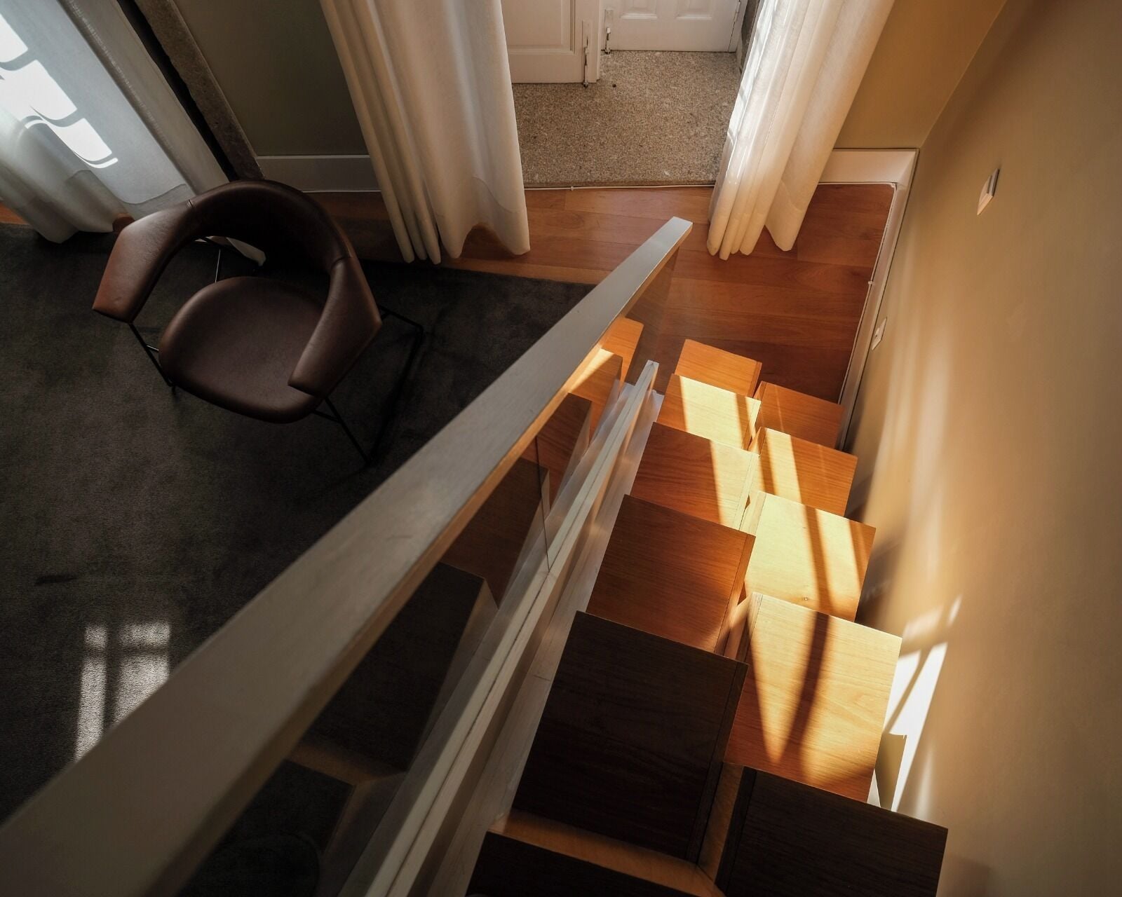 Un interior moderno con una escalera de madera, una silla y vistas a una puerta y cortinas.