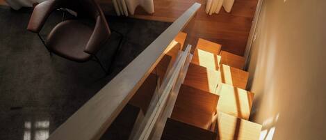 Un interior moderno con una escalera de madera, una silla y vistas a una puerta y cortinas.