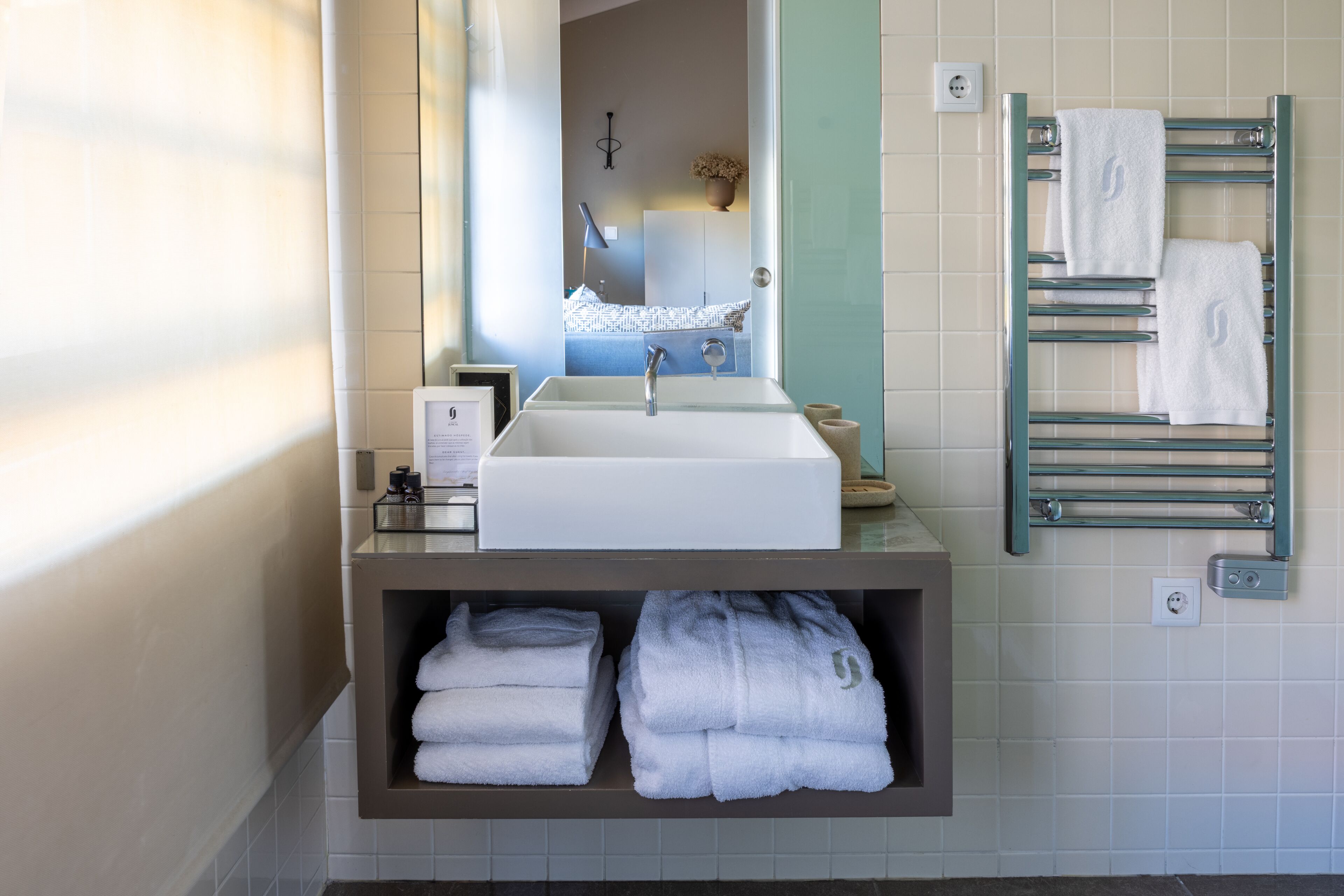 A modern bathroom with a white sink, a towel rack, and a shelf with folded towels.