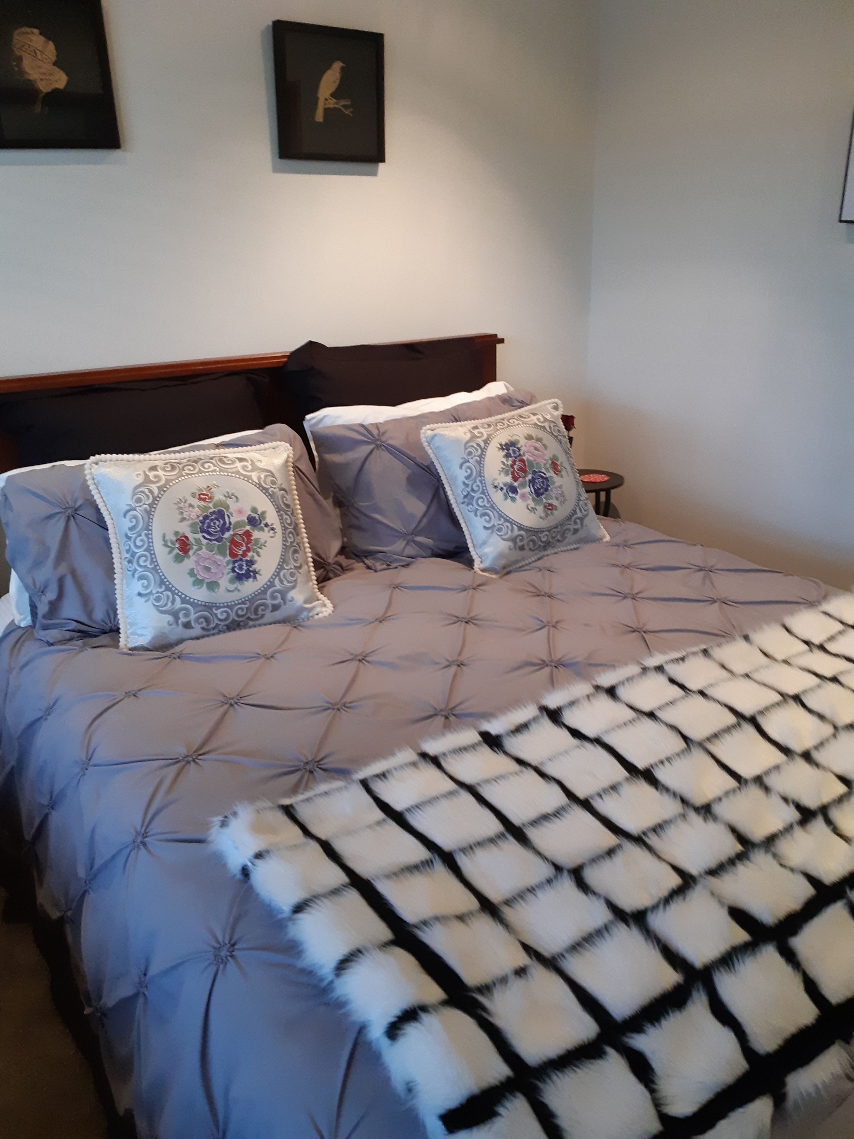 Una cama con cabecera capitonada, dos almohadas decorativas y una manta estampada.