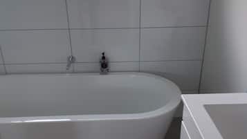 Un baño moderno con una bañera independiente, zona de ducha separada y ventana con vistas a zonas verdes.