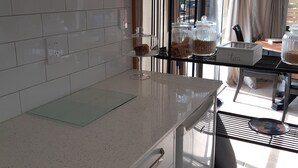 Une cuisine moderne avec des meubles blancs, un four à micro-ondes, un présentoir en verre contenant des produits alimentaires et une machine à café.