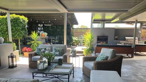 Un espace extérieur aménagé avec des meubles en osier, une table basse et des plantes en pot, le tout abrité.