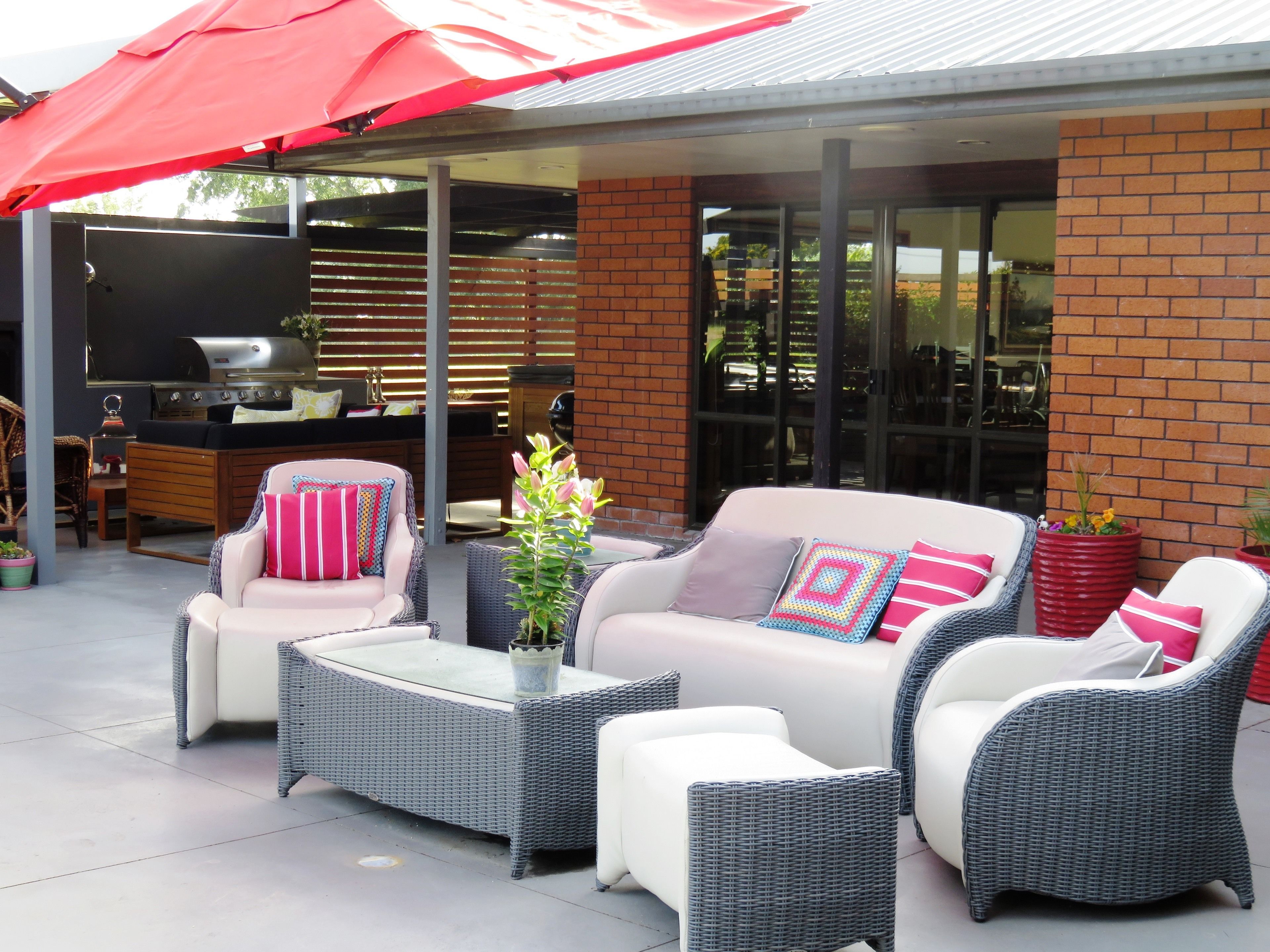 An outdoor patio area with wicker furniture, a red umbrella, and a barbecue grill.