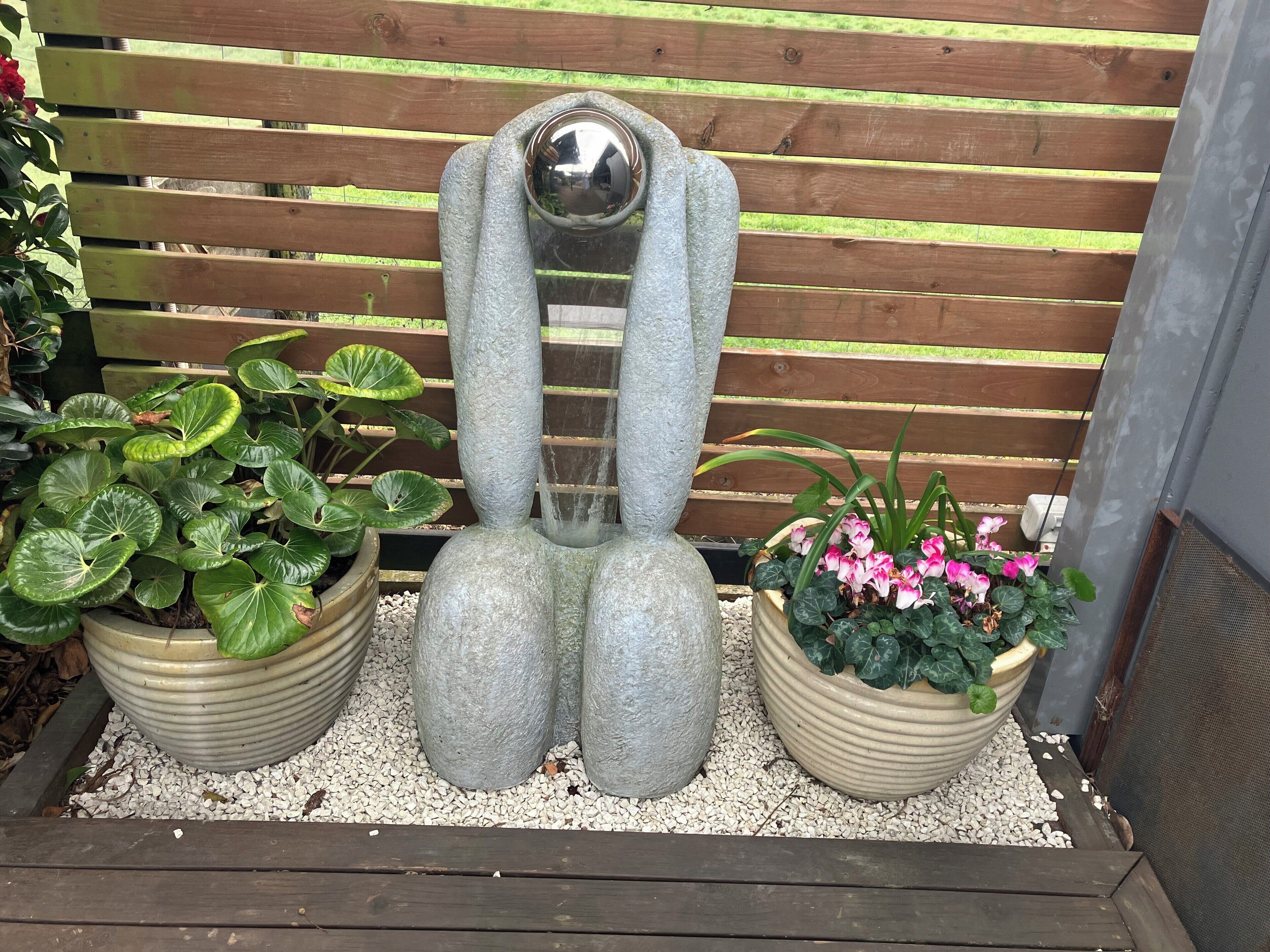 En have med en unik skulptur, plantekrukker og et træhegn.
