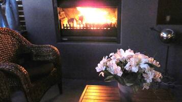 A cozy room with a fireplace, wicker furniture, and a vase of flowers on a wooden table.