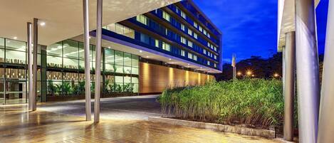 A modern hotel entrance with a glass facade, a wooden deck, and a well-lit outdoor area.