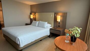 Habitación de hotel con cama, mesitas de noche, una mesa redonda de madera con una planta en maceta y lámparas fijadas a la pared.