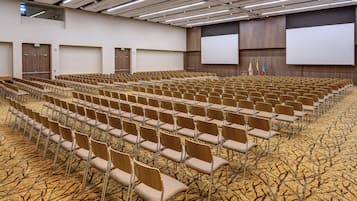 A conference room with rows of chairs, a projector screen, and a carpeted floor.