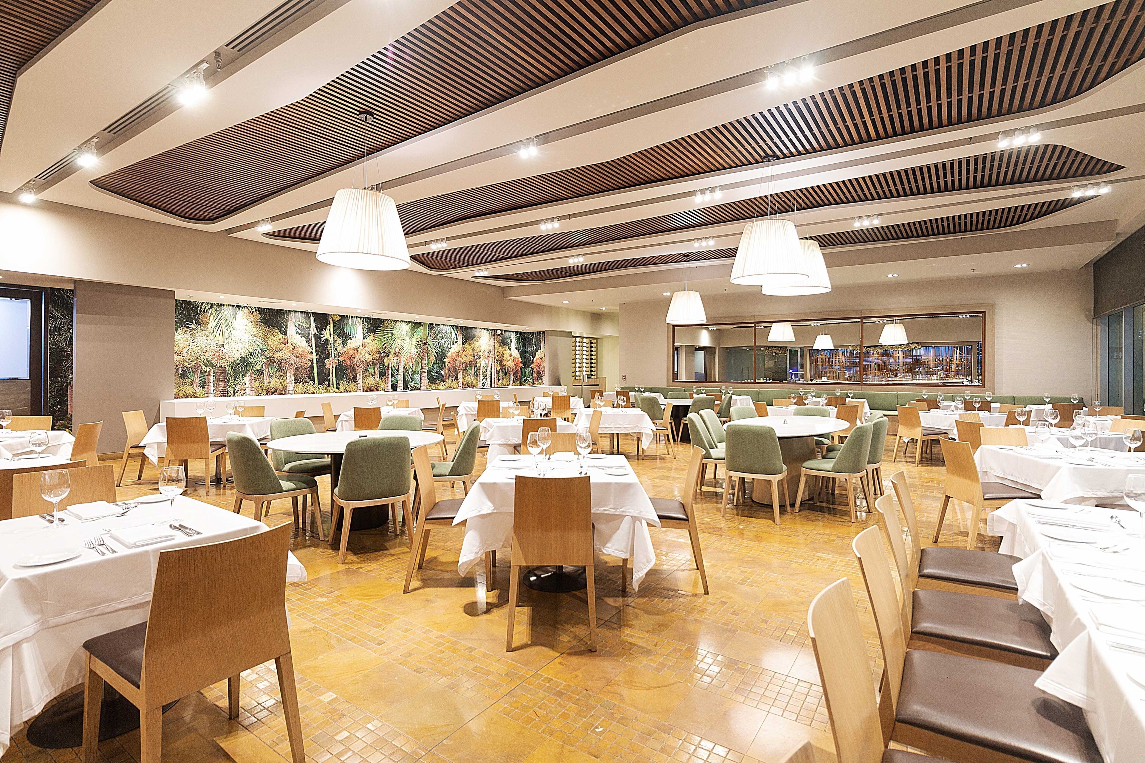 A spacious dining area with multiple tables and chairs, a high ceiling with wooden slats, and pendant lighting.