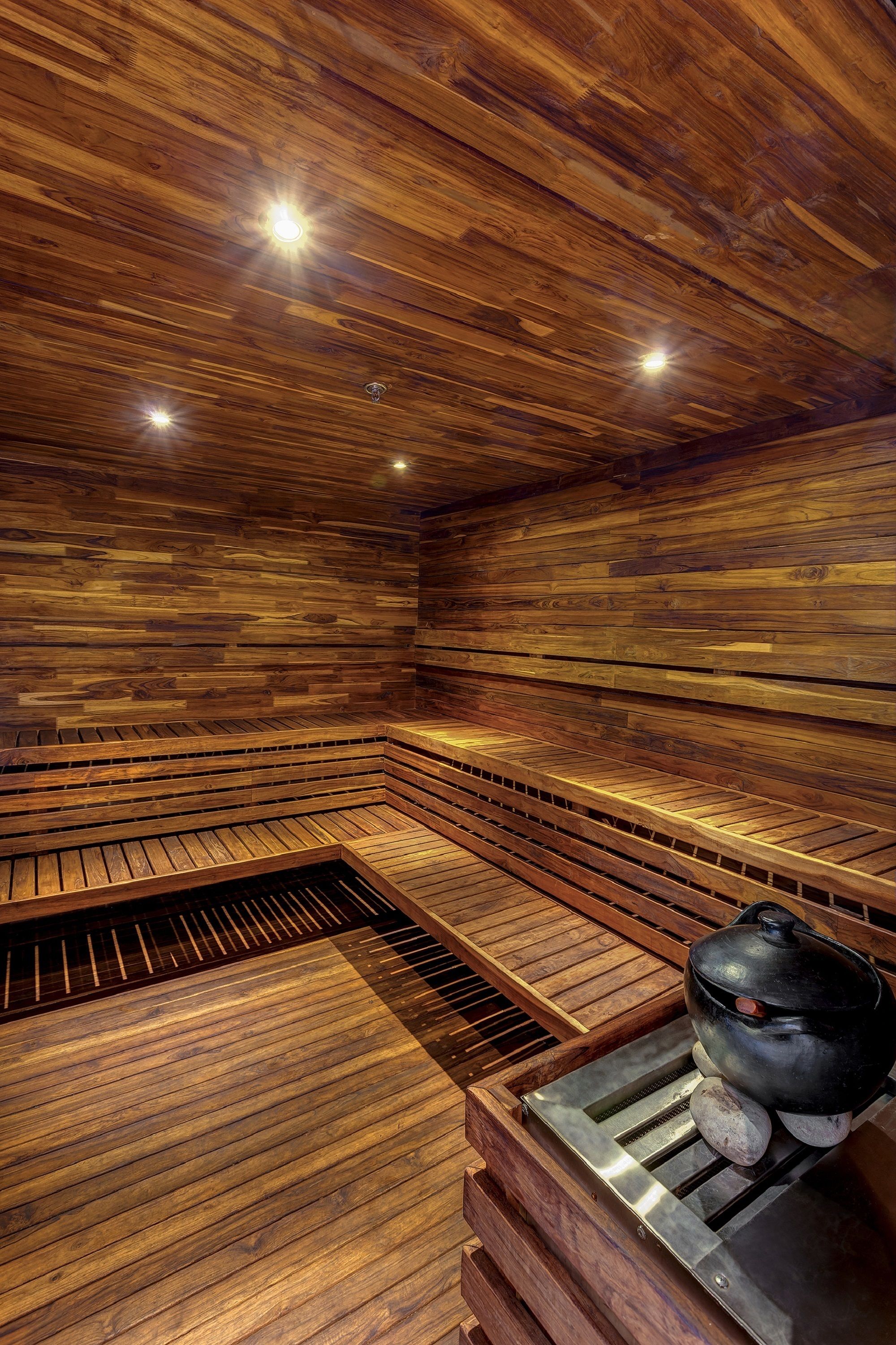 Una sauna con pareti e panche in legno, una griglia metallica e una stufa in pietra.