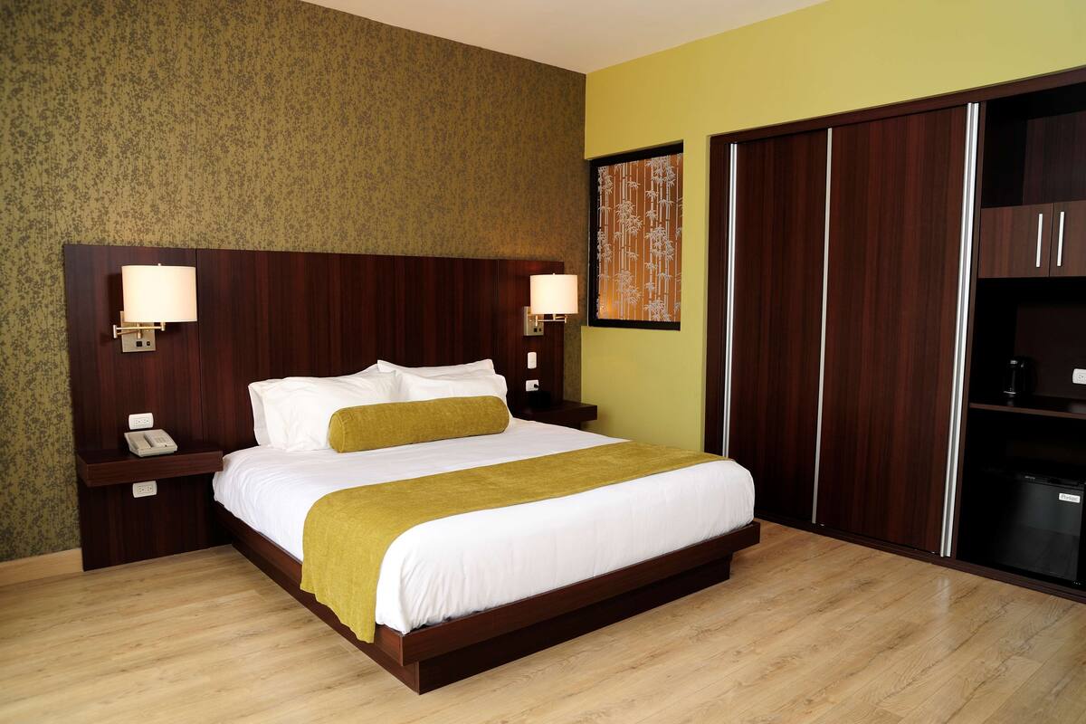 Une chambre d’hôtel avec un grand lit, deux tables de chevet avec des lampes, une armoire et un téléphone fixé au mur.