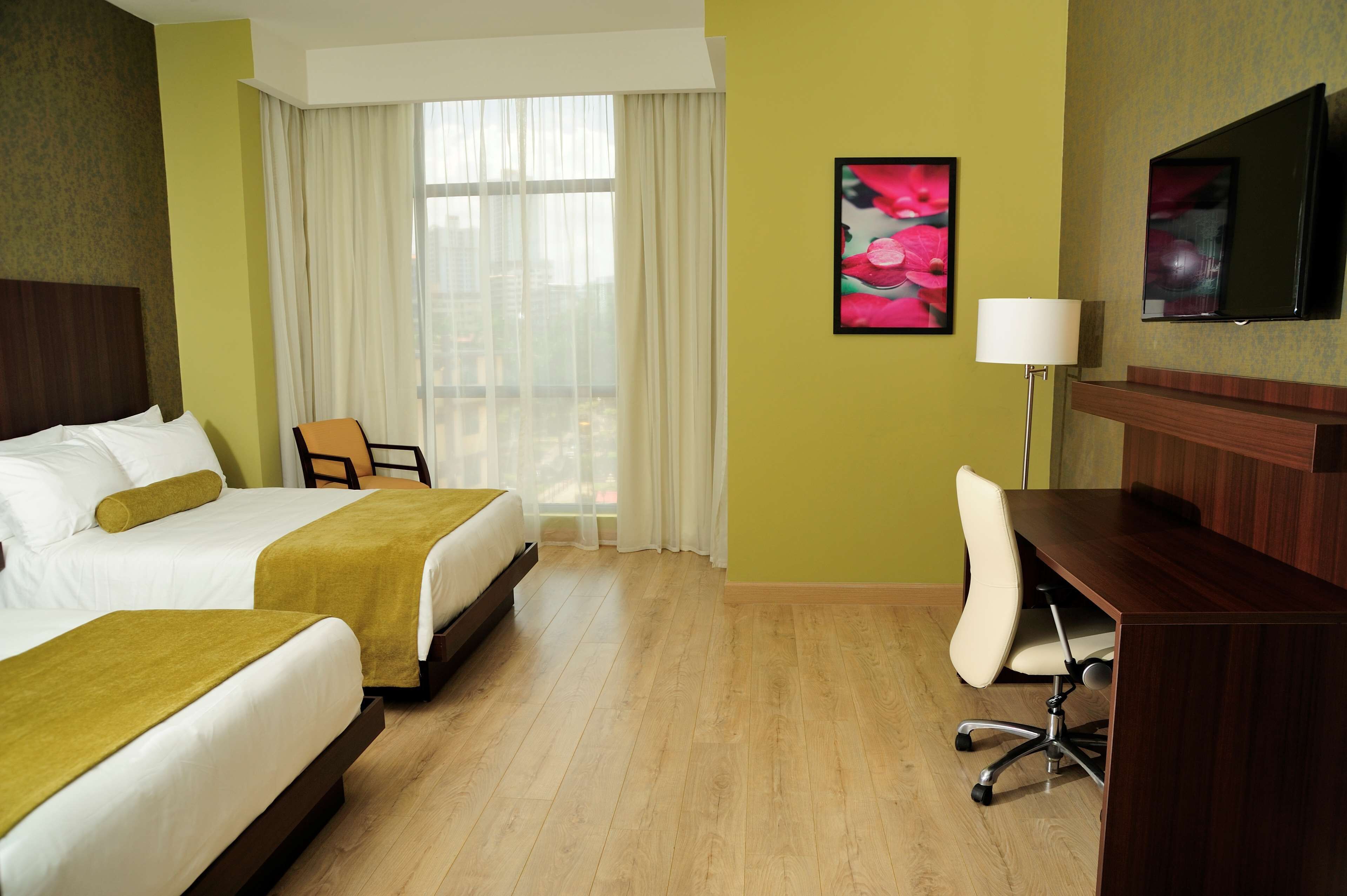 Une chambre d’hôtel avec deux lits, un bureau, une chaise, une télévision et une fenêtre avec des rideaux.