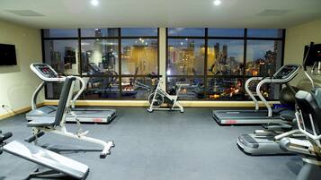 A gym with treadmills, an elliptical, and a stationary bike, featuring a cityscape view through large windows.