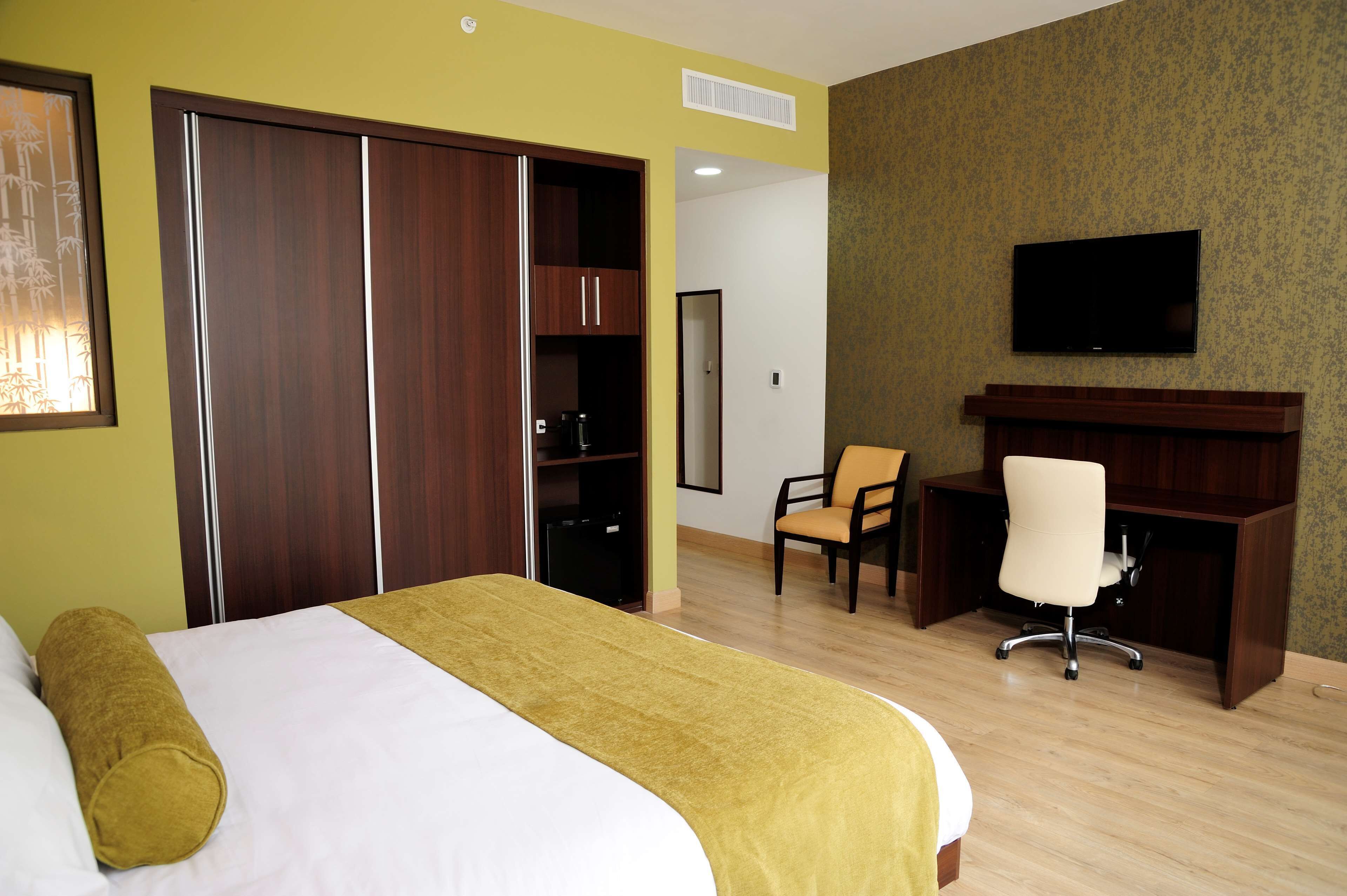 Ein Hotelzimmer mit Bett, Schreibtisch, Stuhl, Fernseher und Kleiderschrank.