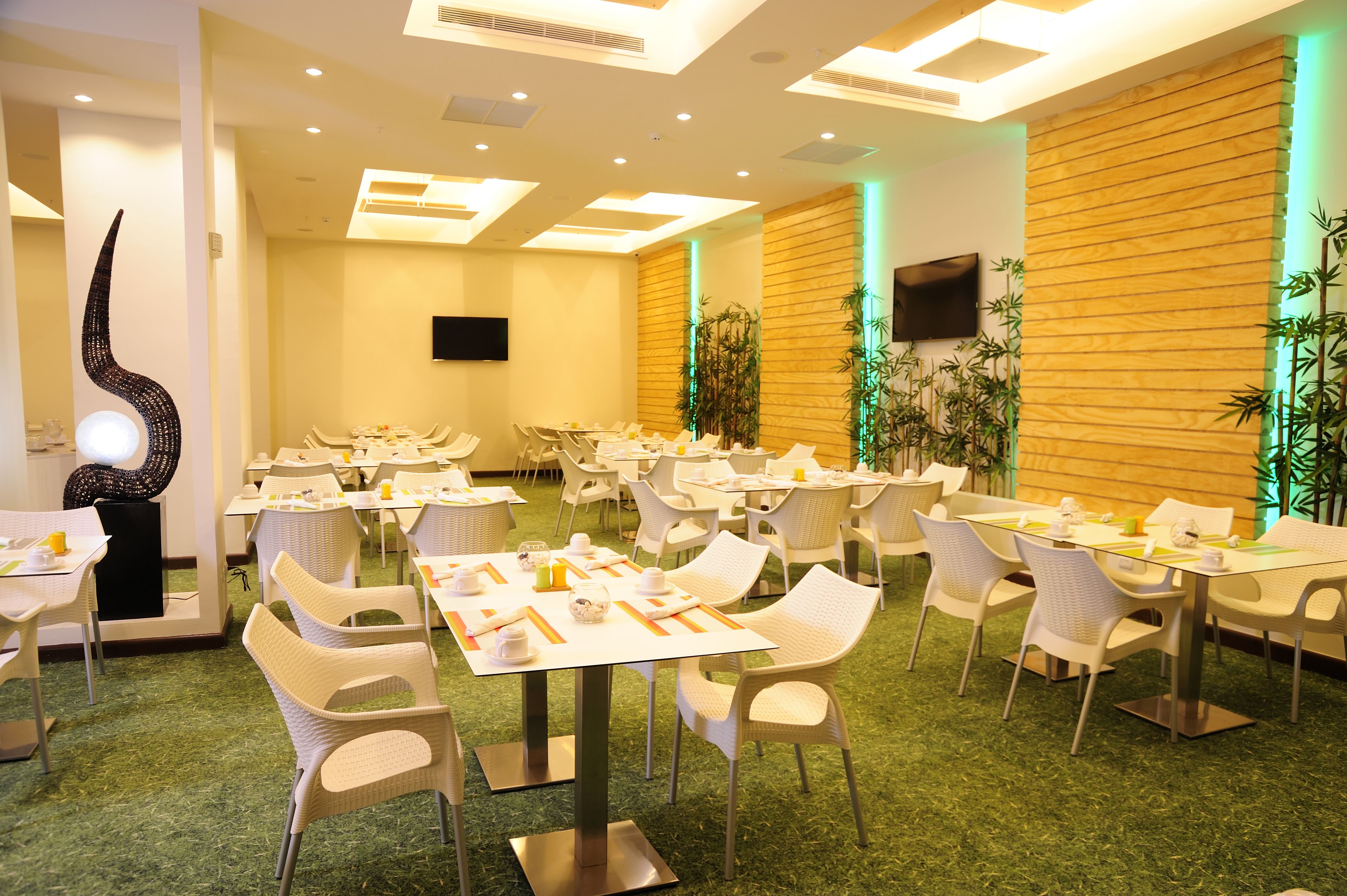 A conference room with multiple tables and chairs, a large sculpture, and a flat-screen TV on the wall.