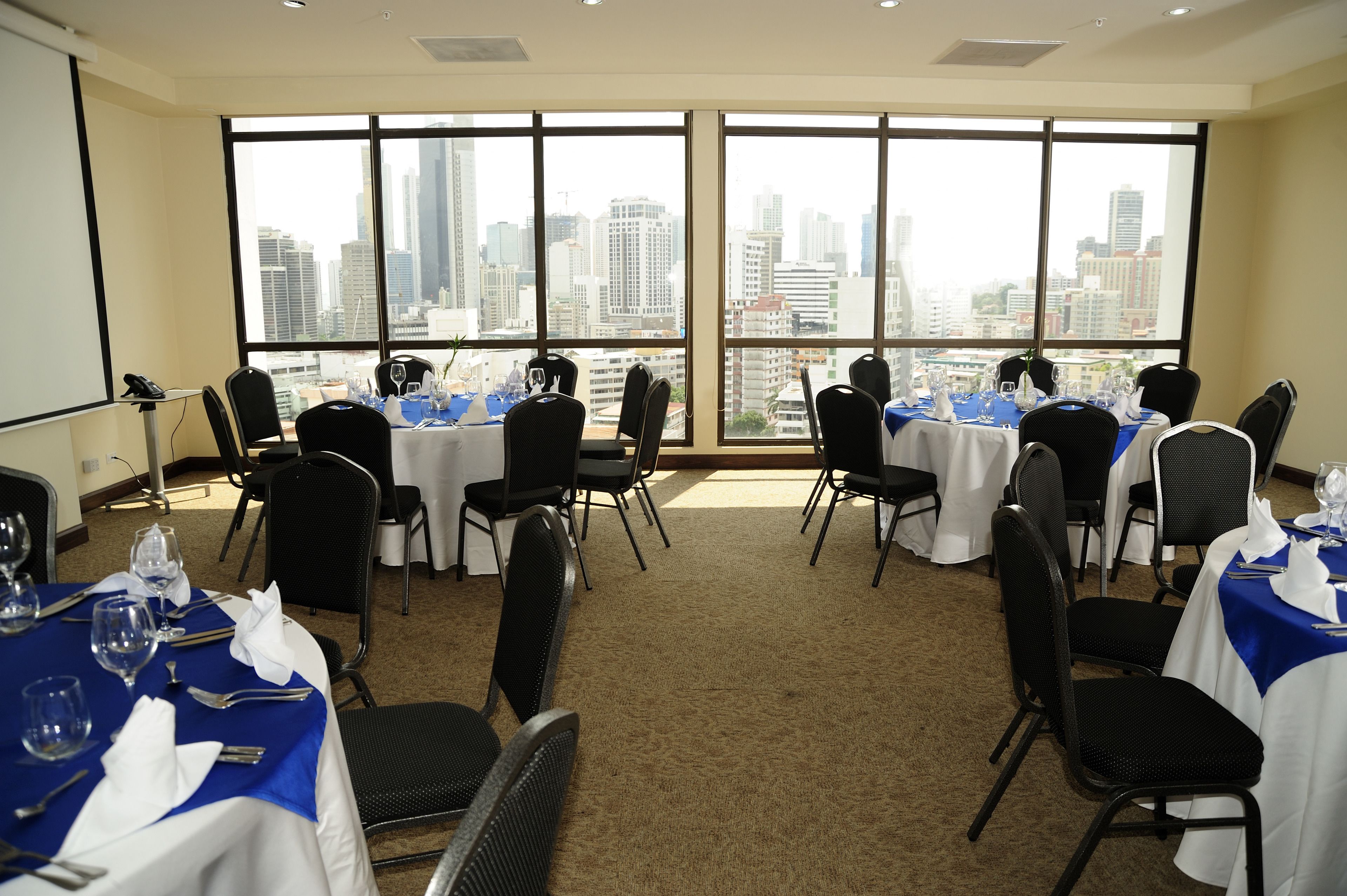 A conference room with tables set for a meeting, large windows with a city view, and a carpeted floor.
