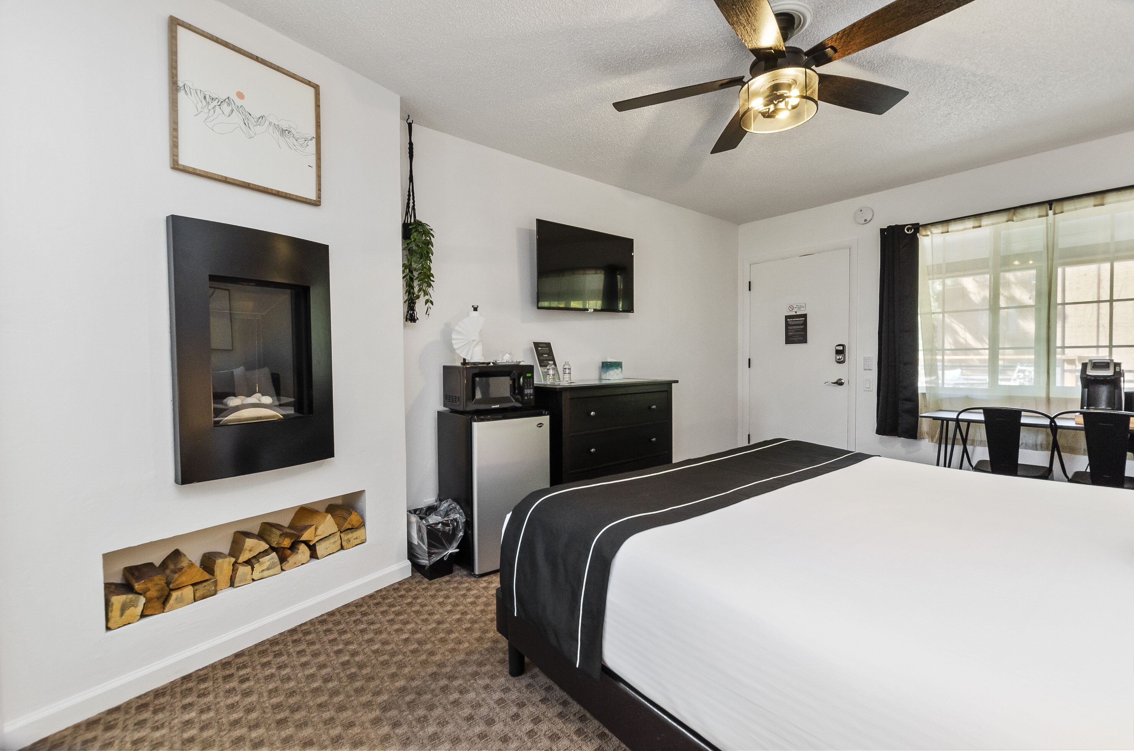 A hotel room with a bed, a desk with a computer, a TV, a ceiling fan, and a window with curtains.