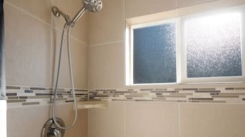 A shower with a handheld showerhead and a wall-mounted faucet, a window with a frosted glass, and a tiled wall with a decorative border.