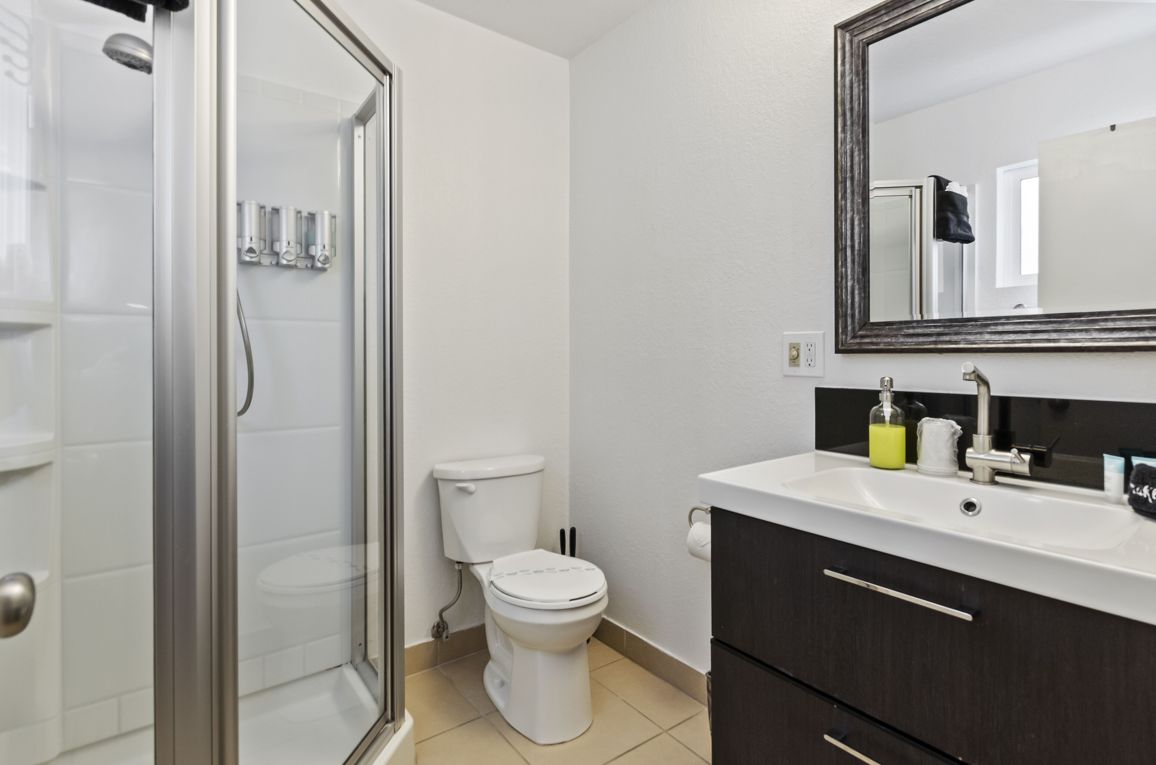 A bathroom with a glass shower enclosure, a white toilet, a sink with a mirror, and dark wooden cabinets.