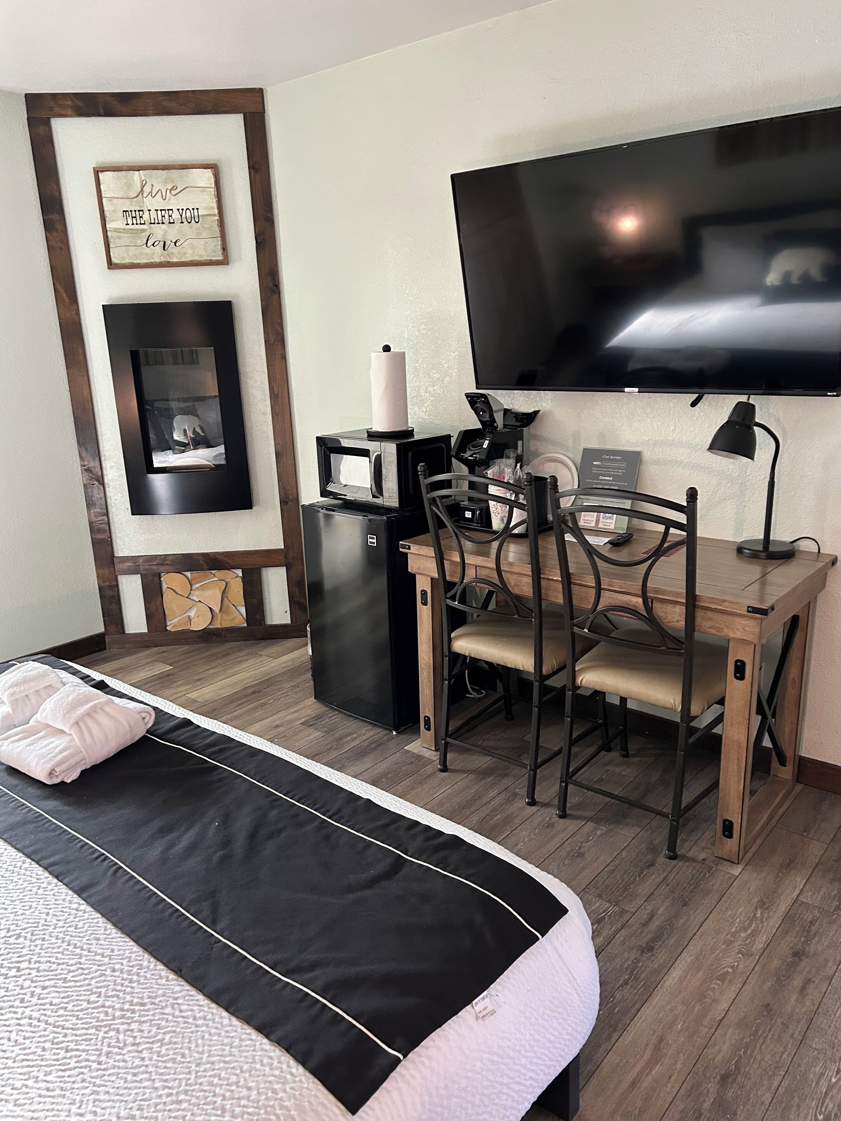 Habitación de hotel con cama, escritorio con computadora, máquina de café, televisor y una cita inspiradora enmarcada en la pared.